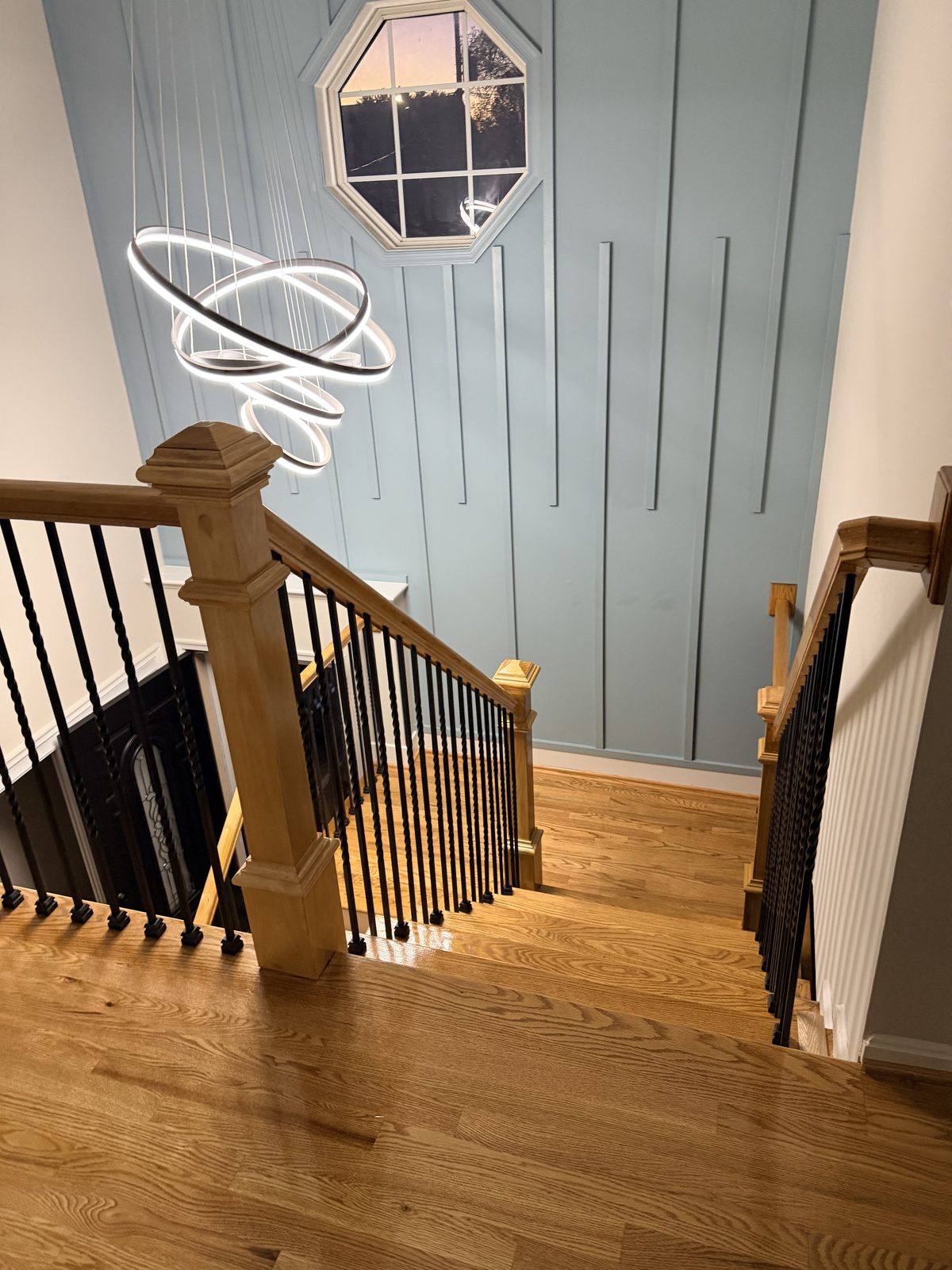 Glossy refinished red oak stair treads seen from the top of the staircase, with a chandelier
