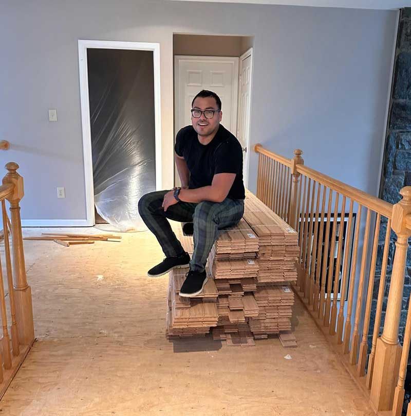 Erlin sitting on a stack of hardwood flooring in a home under renovation
